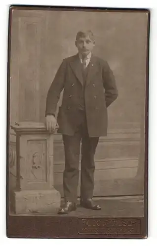 Fotografie Rudolf Tausch, Königs-Wusterhausen, junger blonder Mann im Anzug an Säule stehend
