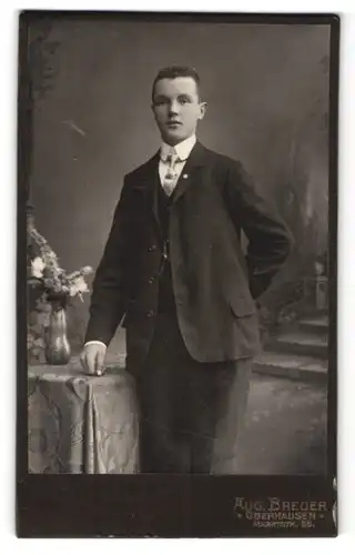 Fotografie Aug. Breuer, Oberhausen, junger Mann im edlen Anzug am Tisch stehend