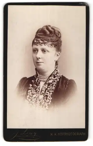 Fotografie J. Löwy, Wien, Portrait hübsche Dame mit Hochsteckfrisur, Perlenhalskette und Bluse mit Stickerei