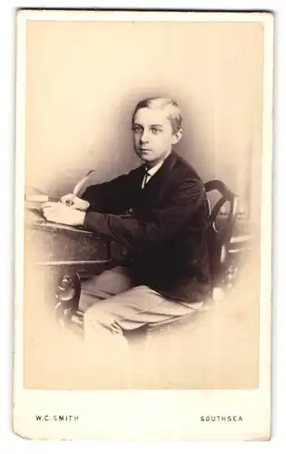 Fotografie W. C. Smith, Southsea, Portrait Knabe mit Schreibfeder am Tisch sitzend