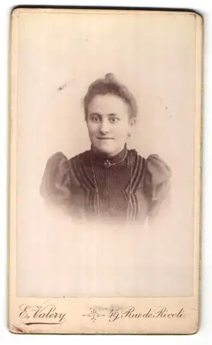 Fotografie E. Valery, Paris, Portrait freundliche junge Frau mit Dutt und Brosche am Kragen