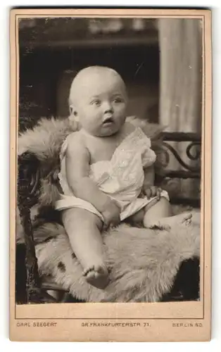 Fotografie Carl Seegert, Berlin, niedliches Kleinkind mit grossen Augen auf Felldecke sitzend