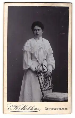 Fotografie E. W. Matthias , Seifhennersdorf, hübsches dunkelhaariges Fräulein im weissen Kleid mit Halskette