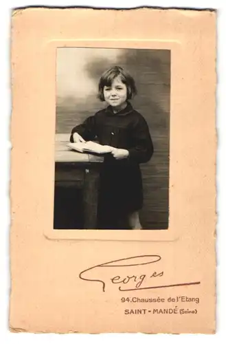 Fotografie Georges, Saint-Mande, niedliches dunkelhaariges Mädchen mit Buch am Tisch stehend