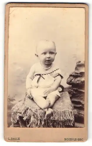 Fotografie L. Dalle, Noisy-le-Sec, Kleinkind mit Perlenkette auf Mauer sitzend