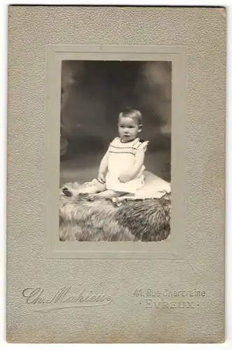 Fotografie Mahieu, Evreux, kleines Kind in weissem Hemdchen sitzt auf einem Fell