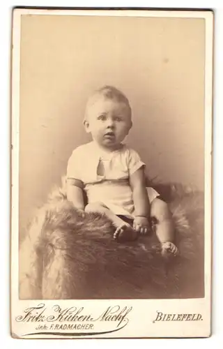 Fotografie Fritz Küken Nachf., Bielefeld, Portrait niedliches blondes Kleinkind auf einem Fell