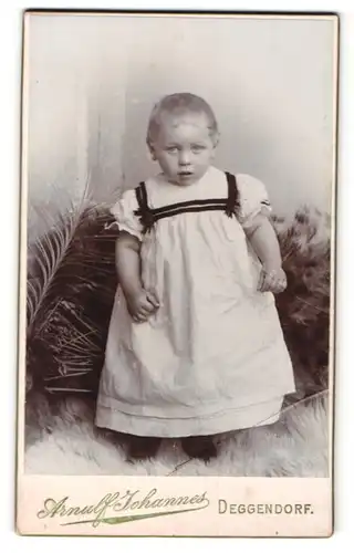 Fotografie Arnulf Johannes, Deggendorf, niedliches blondes Kleinkind im weissen Kleidchen mit schwarzen Schleifen