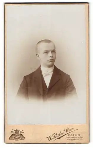 Fotografie Wilhelm Stein, Berlin, Portrait junger Mann mit kurzem Haar und weisser Fliege im Anzug