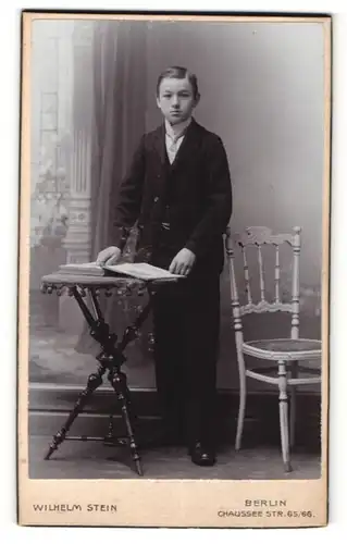 Fotografie Wilhelm Stein, Berlin, Portrait Knabe mit Buch am Tisch