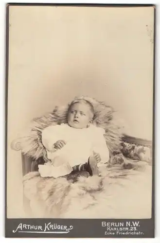 Fotografie Arthur Krüger, Berlin, süsses blondes Kleinkind mit hübschen Stiefelchen auf Felldecke liegend
