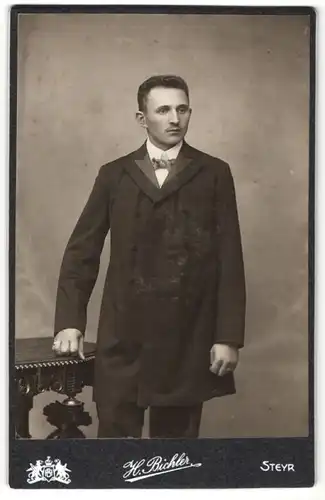 Fotografie H. Bichler, Steyr, junger dunkelhaariger Mann mit oberlippenbart im eleganten schwarzen Mantel