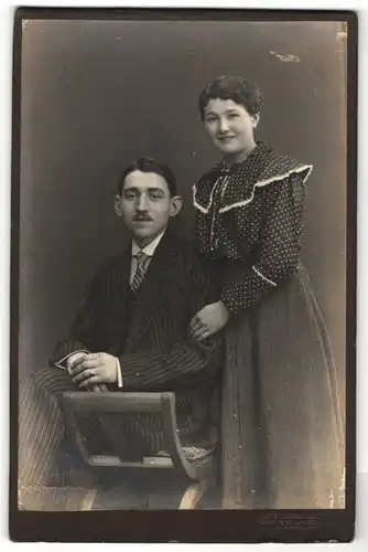 Fotografie R. Rosenkranz, Mügeln, lächelndes Fräulein in gepunkteter Bluse & junger Mann mit Schnauzer im Streifenanzug