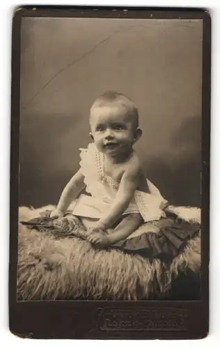 Fotografie Otto Reinicke, Leipzig-Paunsdorf, süsses blondes Kleidnkind im weissen Hemdchen auf Felldecke sitzend