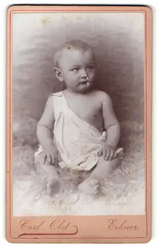 Fotografie Carl Obst, Erkner, zuckersüsses blondes Kleinkind mit nackten Füssen auf Felldecke sitzend