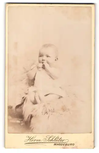 Fotografie Herm. Schlüter, Magdeburg, Baby in weissem Kleid auf einem Fell