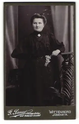 Fotografie G. Sauer, Wittenberg, charmant lächelnde Dame im schwarzen Kleid mit Blume in der Hand