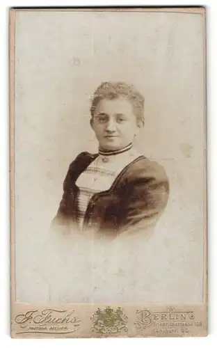 Fotografie J. Fuchs, Berlin, Portrait lächelnde junge Frau mit Brosche in elegant bestickter Bluse