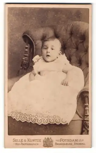 Fotografie Selle & Kuntze, Potsdam, Baby im Kleidchen auf Sessel sitzend