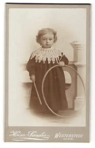 Fotografie Heinr. Sander, Westerstede i/Oldb., Portrait Kleinkind mit Holzreifen