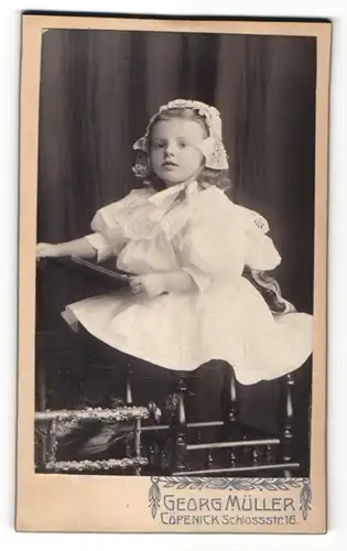 Fotografie Georg Müller, Berlin-Köpenick, zuckersüsses kleines Mädchen im weissen Kleid mit gerüschter Mütze und Buch