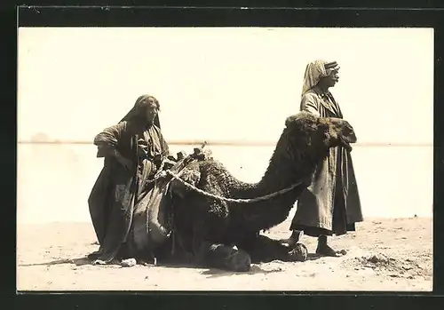 Foto-AK Araber und seine Frau mit liegendem Kamel im Sand, arabische Volkstypen