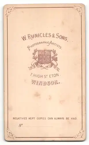 Fotografie Atelier W. Runicles & Sons, Windsor, stehende Frau mit dunkler Jacke und hellem Hut auf Hocker gelehnt