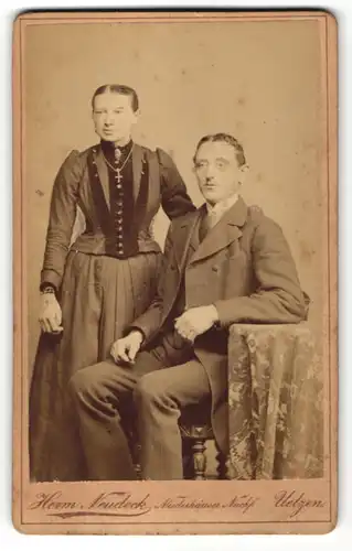 Fotografie Herm. Neudeck, Uelzen, Herr im Anzug sitzend neben Frau im Kleid stehend