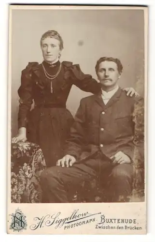 Fotografie H. Siggelkow, Buxtehude, sitzender Mann und stehende Frau mit ihrem Arm auf der Schulter