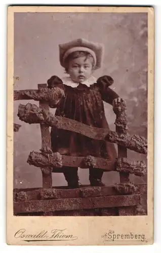 Fotografie Oswald Thiem, Spremberg, zuckersüsses Mädchen mit Hut im Kleid am Holzzaun stehend