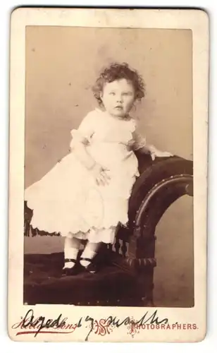 Fotografie Hellis & Sons, London, zuckersüsses kleines Mädchen mit lockigem Haar im weissen Rüschenkleid