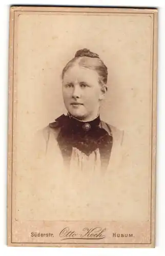 Fotografie Otto Koch, Husum, Portrait blondes Fräulein mit Hochsteckfrisur und Brosche am schwarzen Kragen