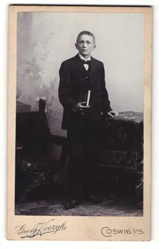 Fotografie Georg Koczyk, Coswig i. S., Portrait blonder hübscher Bube mit Buch im schwarzen Anzug