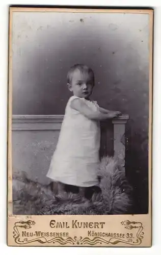 Fotografie Emil Kunert, Neu-Weissensee, Portrait Kleinkind im weissen Kleid auf einem Fellteppich