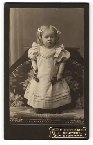 Fotografie C. Fettback, Salzwedel, Portrait kleines Mädchen mit Haarschleifchen auf einer Bank