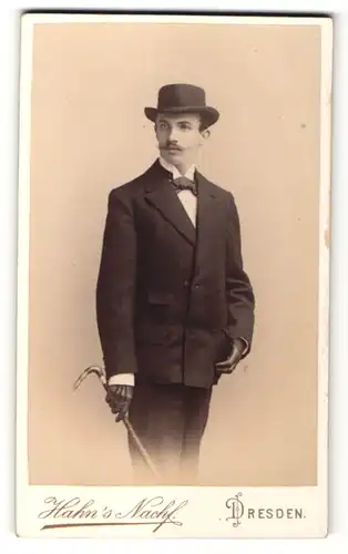 Fotografie Hahn's Nachf., Dresden, Portrait eleganter junger Mann mit Hut, Stock und Handschuhen im Anzug