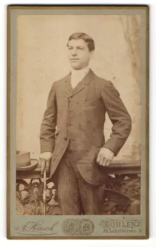 Fotografie A. Kirsch, Coblenz, Portrait junger dunkelhaariger Mann mit Scheitel und Stock in gestreifter Anzughose