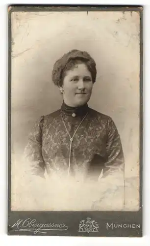 Fotografie M. Obergassner, München, Portrait charmant lächelnde Dame in elegant bestickter Bluse mit Ohrringen