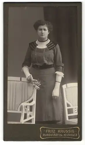 Fotografie Fritz Krussig, Burgstädt i. Sa., dunkelhaarige junge Schönheit mit Blume und Halskette im bestickten Kleid