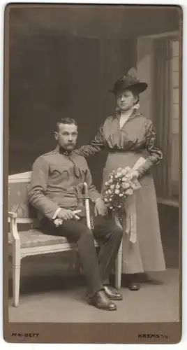 Fotografie M.K. Bett, Krems a. D., österreichischer Soldat in Uniform mit Säbel und Gattin im Foto-Atelier