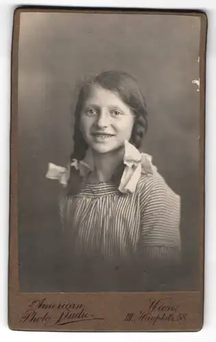 Fotografie American Photo-Studio, Wien, Portrait lachendes Mädchen mit Flechtzöpfen und Haarschleifen