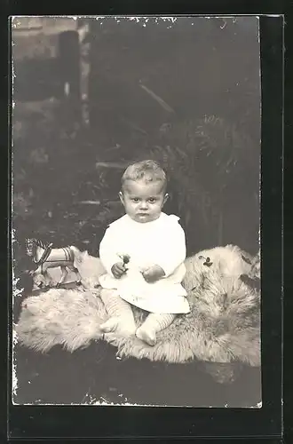 AK Baby auf einem Fell mit Holzpferchen sitzend