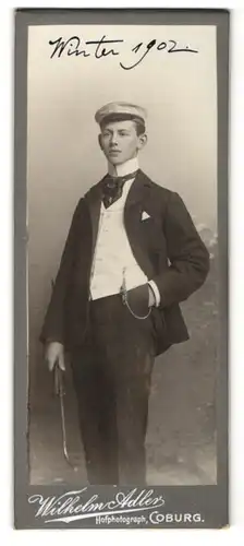 Fotografie Wilhelm Adler, Coburg, Student im Anzug mit Krawatte & Spazierstock, Winter 1902