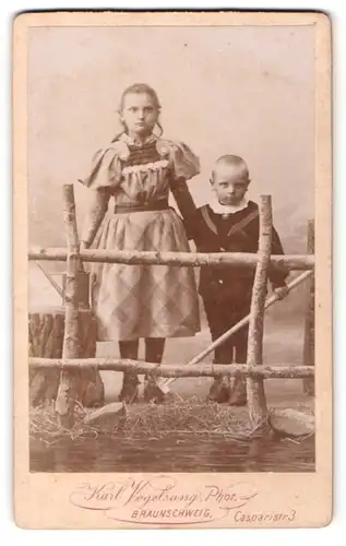 Fotografie Karl Vogelsang, Braunschweig, Portrait Mädchen im karierten Kleid und Brüderchen am Zaun stehend