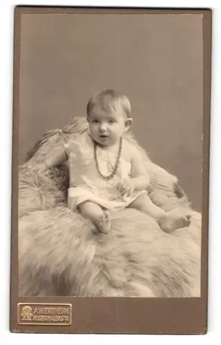 Fotografie A. Wertheim, Berlin, Portrait kleines Mädchen im weissen Hemd mit Perlenkette auf Fell sitzend