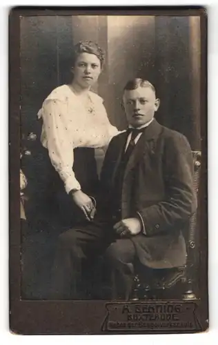 Fotografie A. Behning, Buxtehude, Portrait junger Herr im Anzug auf einem Stuhl sitzend mit seiner Frau