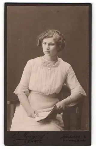 Fotografie L. Margraf, Lehrte, Portrait junges hübsches Mädchen in weisser Bluse mit Zeitung auf einem Stuhl sitzend