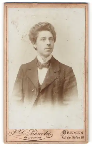 Fotografie F. D. Schrader, Bremen, Portrait junger Herr mit Locken und Fliege im Anzug