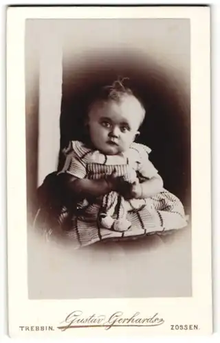 Fotografie Gustav Gerhards, Zossen, Portrait Kleinkind im zeitgenössischen Kleid auf einem Stuhl sitzend