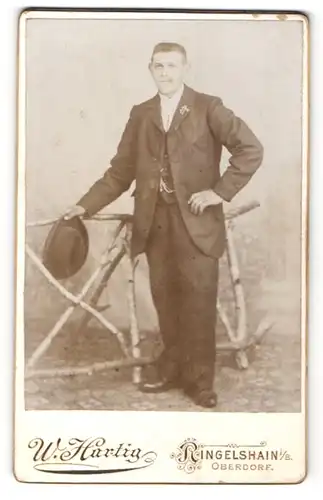 Fotografie W. Hartig, Ringelshain i / B., Portrait junger bürgerlicher Herr mit Hut im Anzug an Zaun gelehnt